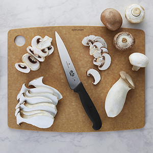 A straight edge Fibrox knife on a cutting board surrounded by sliced mushrooms