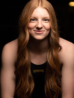 Lydia Jacoby wearing an arena racing suit in black and gold, smiling at the camera
