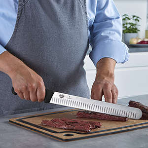 A man using a Fibrox knife to slice meat on a cutting board