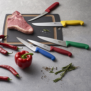 Multicolored Fibrox knives on a cutting board with a piece of steak and peppers